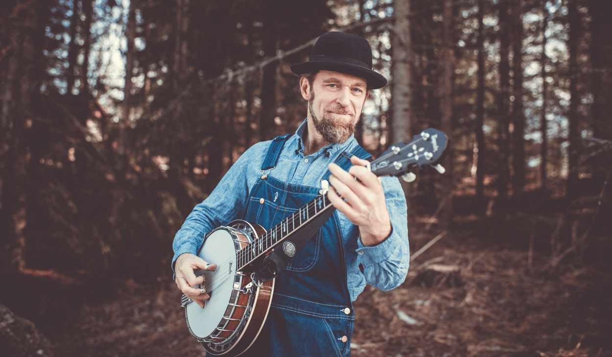 En man i overall som spelar gitarr i skogen.
